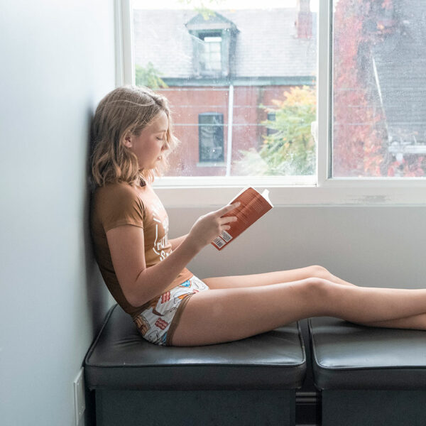 a girl sitting in a window seat reading a book while wearing a brown shirt and comfortable brief underwear