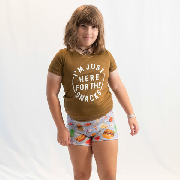 girl posing on a white backdrop in boxers and a t-shirt.