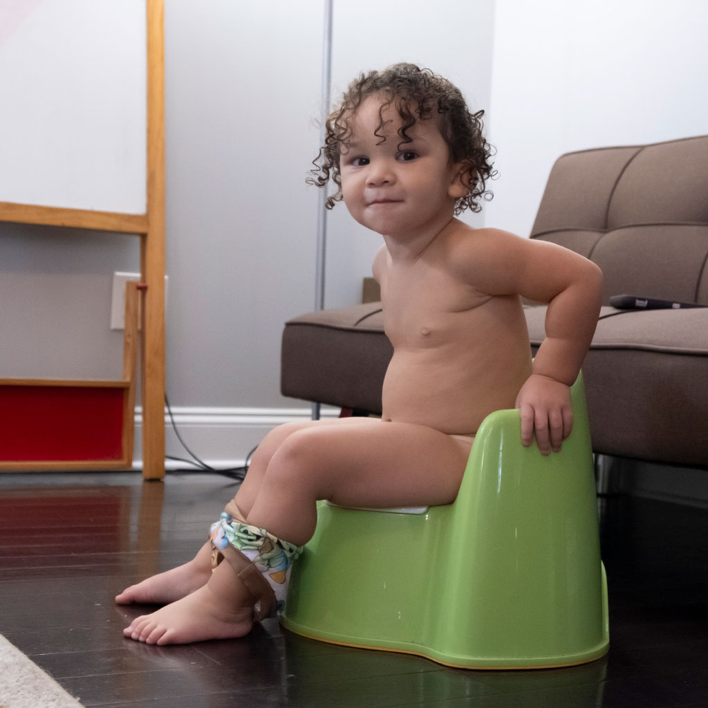 a toddler girl sitting on a little green froggy potty